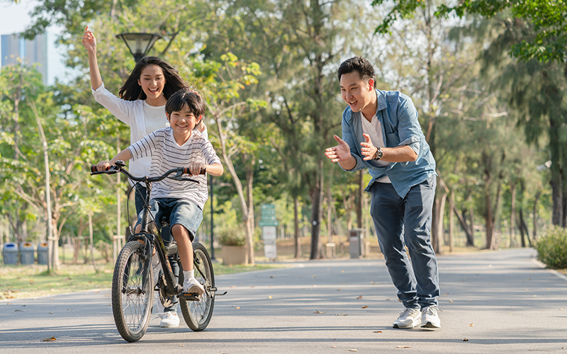 Happy Asian family father and mother teaching their son to ride bicycle at the park