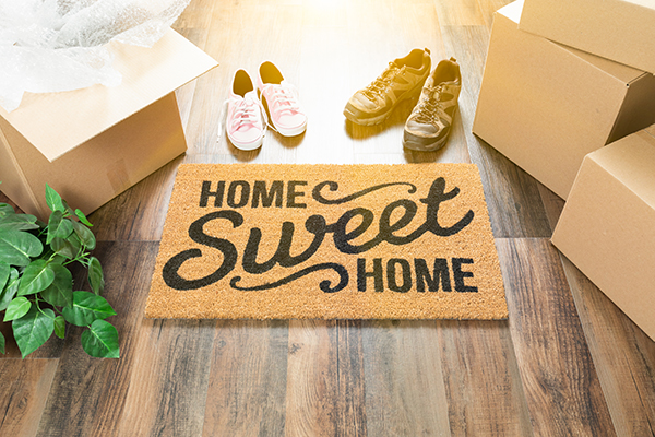 Home Sweet Home Welcome Mat, Moving Boxes, Women and Male Shoes and Plant on Hard Wood Floors